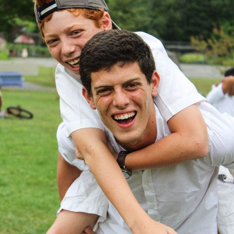 male staff giving male camper a piggy back ride+smiling